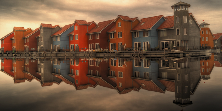 Row of colourful houses perfectly reflected in still water, symbolising reciprocity and mirrored behaviour